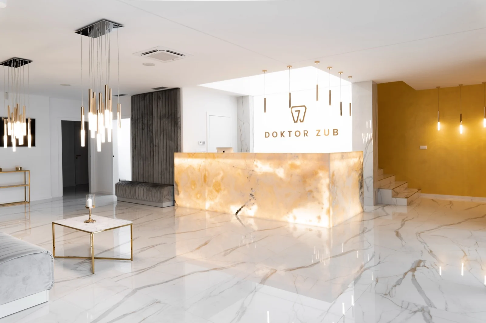Reception area of the Doktor Zub dental clinic, with a backlit onyx desk, marble floor and brass pendant lights